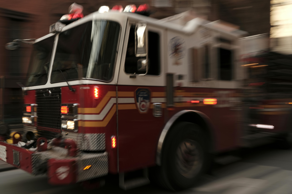 Dynamic image of a red fire truck speeding through the streets of New York City.
