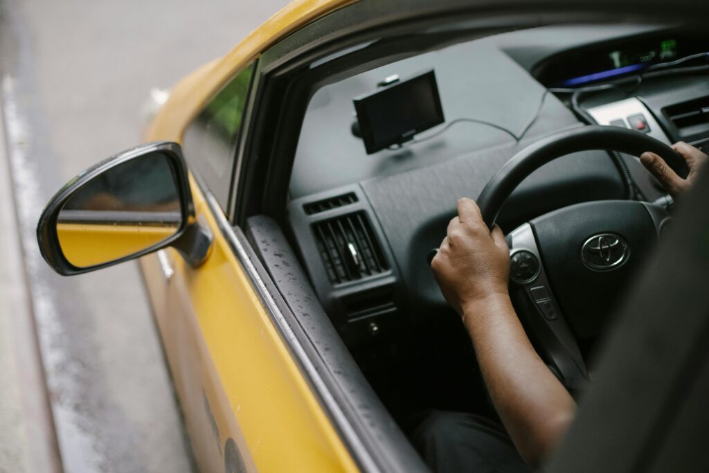 From above of crop unrecognizable person driving modern yellow taxi car with GPS navigator on city street in daytime