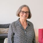 Charming senior woman with eyeglasses smiling warmly at home in a relaxed indoor setting.