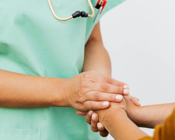A nurse in green scrubs gently clasps a patient's hand, offering support.