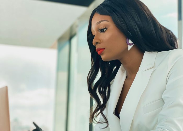 Elegant African American woman in white blazer working on a laptop in a modern office.