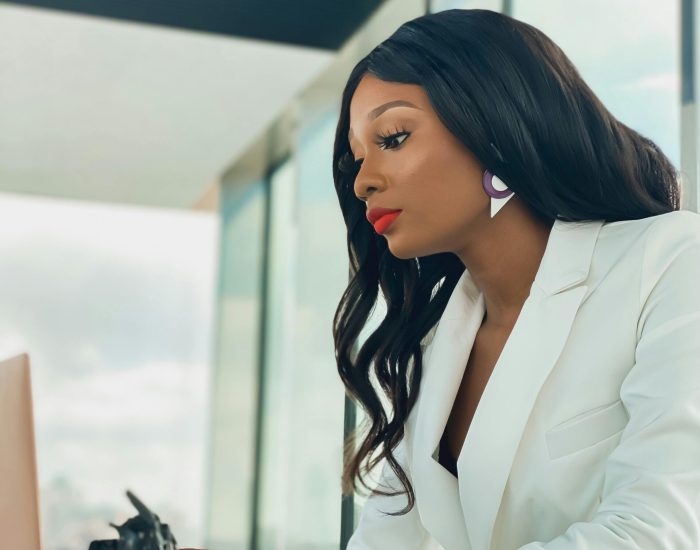 Elegant African American woman in white blazer working on a laptop in a modern office.
